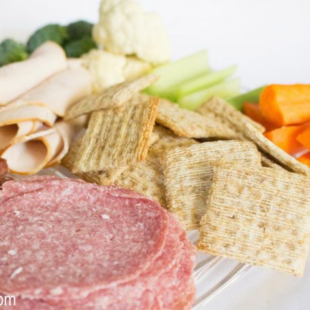 Cold cuts, crackers and fresh vegetables on a white plate