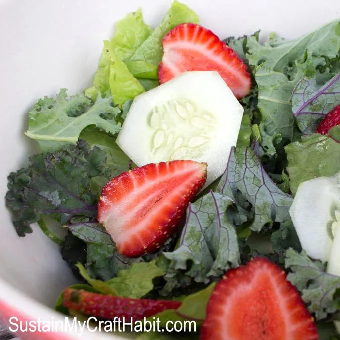 Salad bowl filled with slices cucumbers, strawberries, kale and greens.