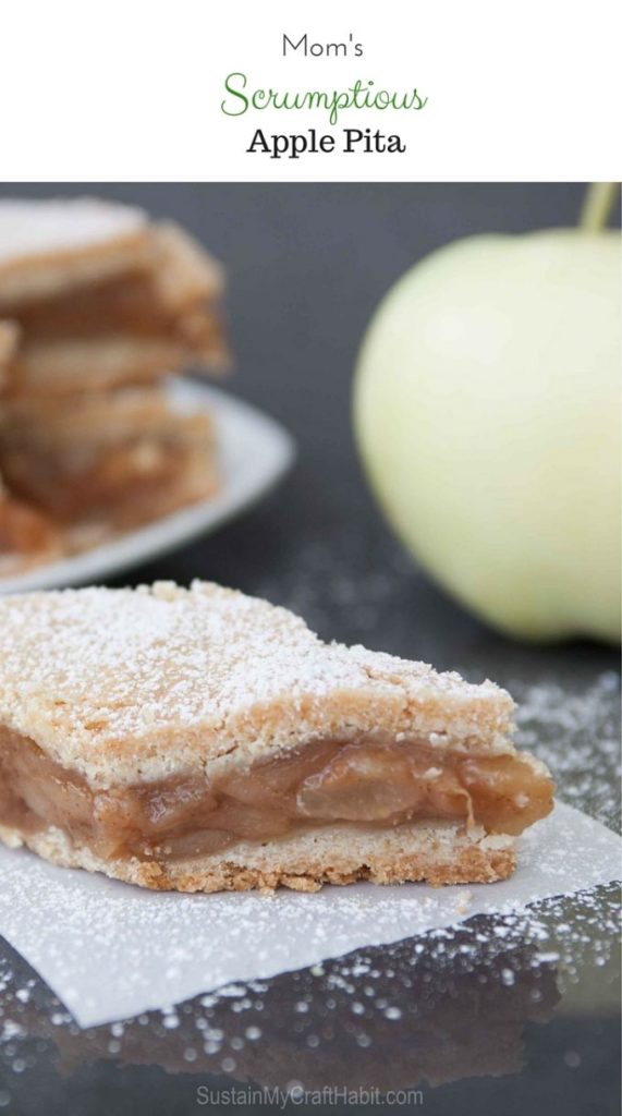 A small piece of apple pita pie, sprinkled with powdered sugar on a piece of parchment paper on a dark gray surface.