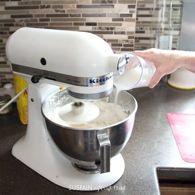 Pouring yeast and warm water into a Kitchen Aid mixer bowl filled with flour to make a simple white bread recipe