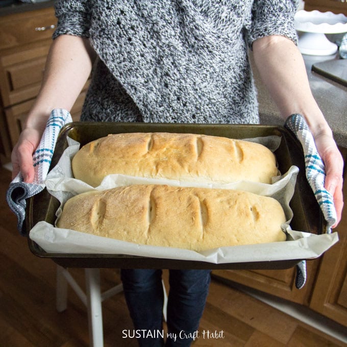 Woman holding two fresh baked loaves of white bread on a baking sheet made from this easy bread recipe