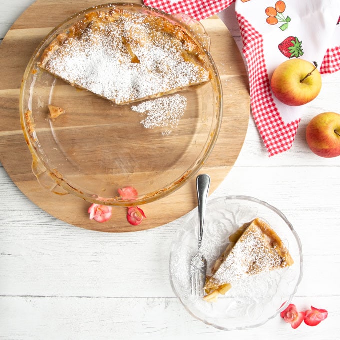 An overhead shot of the cinnamon apple rhubarb pie on a round wooden cutting board surrounded by fresh apples. 