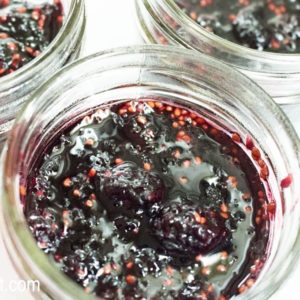 Close up image of deep red homemade mulberry jam in a small glass jar.