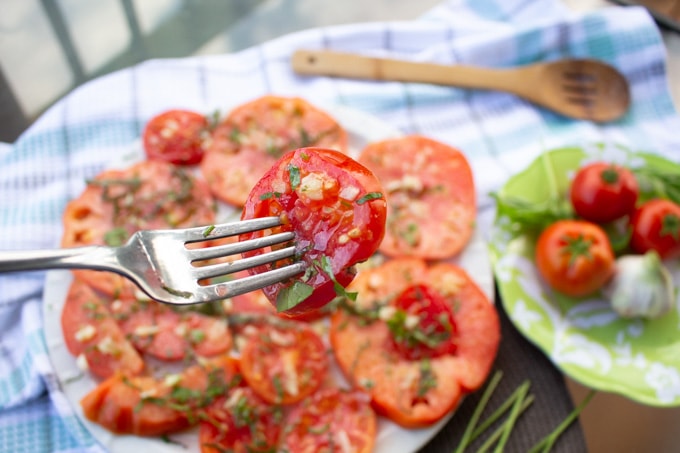 Small slice of tomato salad on a fork with a plate full of the slices in the background.