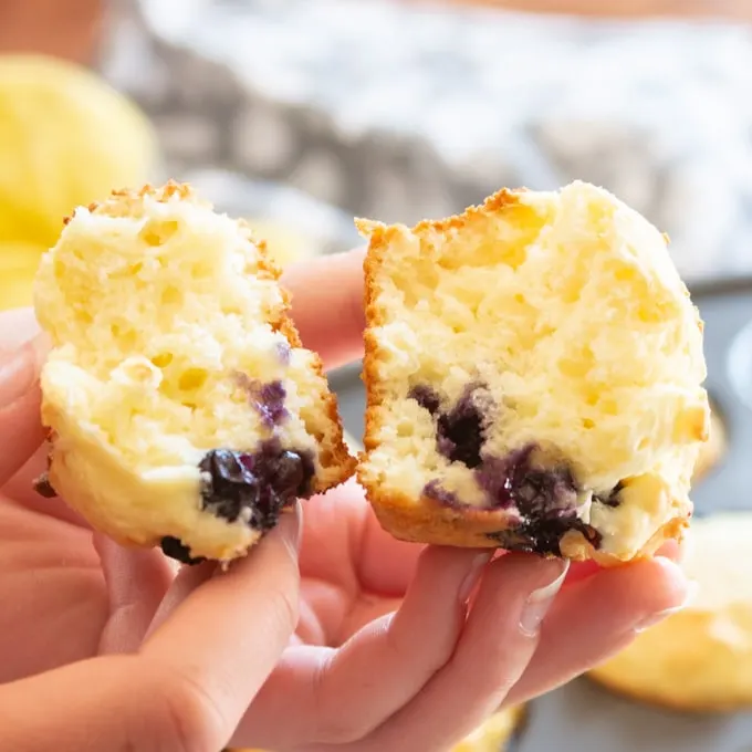 Close up image of someone holding a blueberry muffin made with sour cream, broken in half to show the inside.