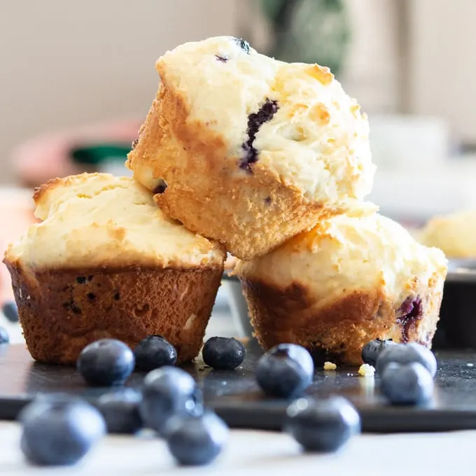 Stack of baked muffins surrounded by fresh blueberries.