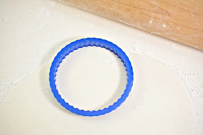 A blue scalloped cookie cutter on the rolled out fondant.