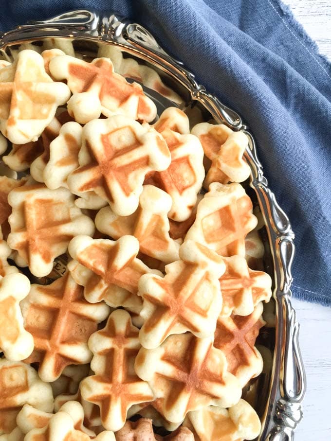 A silver platter filled with bite-sized waffle cookies. A blue napkin is in the background.