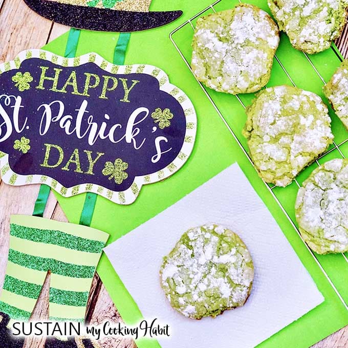 Close up image of the baked green crinkle cookies beside and sign which says Happy St. Patrick's Day.