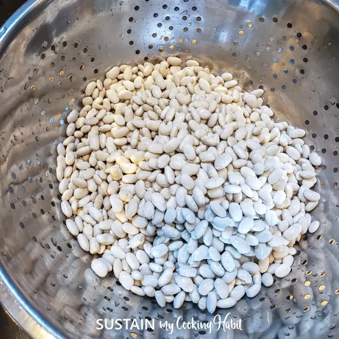 Rinsing dried white beans in a steel collander.