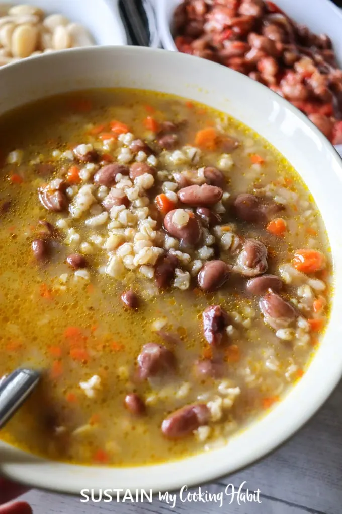 A white serving bowl filled with beans and barley soup.