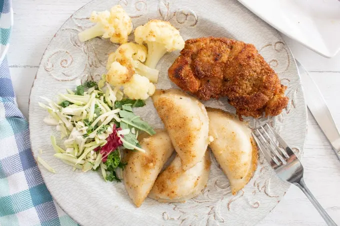 Overhead view of a round plate with with the cooked frozen perogies recipe, breaded chicken, cauliflower and coleslaw.