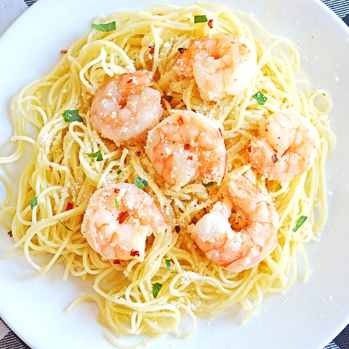 Overhead image of a bed of pasta topped with cooked shrimp and sprinkled with fresh parsley on a white plate.