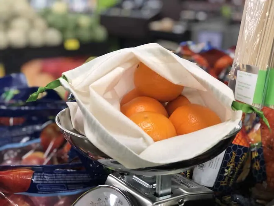 An open cloth produce bag with oranges inside.