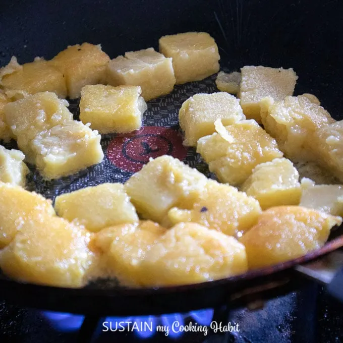 Polenta cubes being seared on a stove-top skillet.