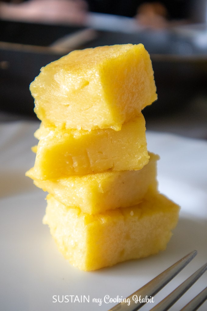 Close up image of four cubes of fried polenta stacked on top of each other on a white plate.