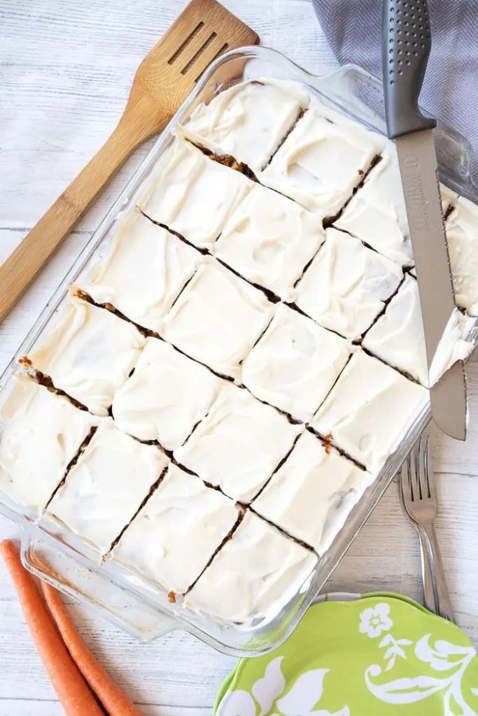 Overhead view of a carrot cake in a rectangular glass dish with white frosting. The carrot cake has been cut into 20 serving size squares.