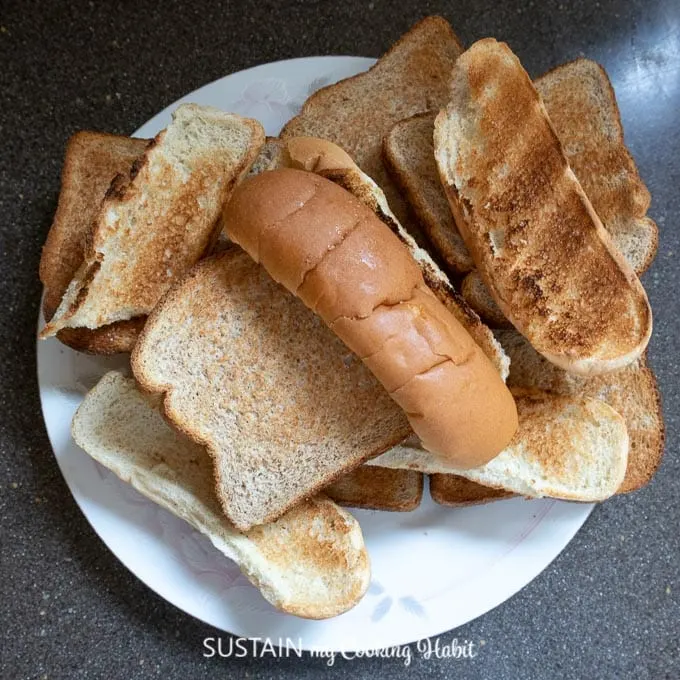 A plate filled with a variety of dried and stale breads including hot dog buns and sandwich bread.