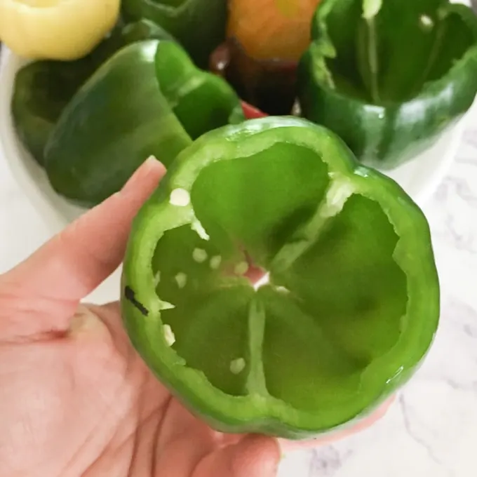 Woman holding green pepper with top sliced off and seeds removed. 