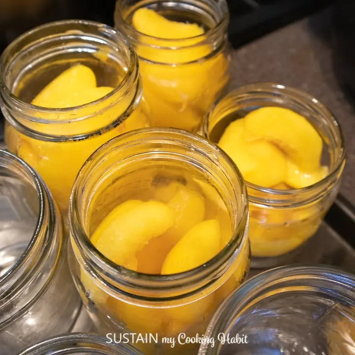 Covering the peaches by pouring syrup into the mason jars.