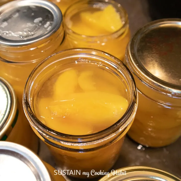 Close up of canned peaches in a jar with some jars sealed at the top.