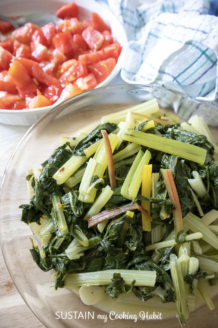 Platter of cooked Swiss chard and garlic as a side dish next to a platter of chopped tomatoes.