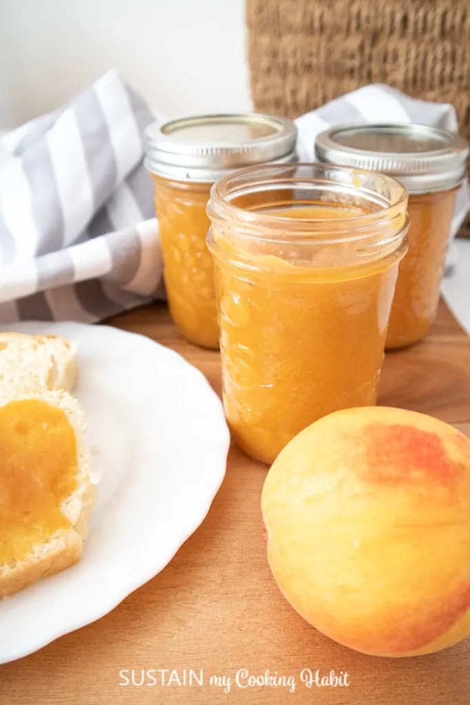 Finished low-sugar peach jam next to a fresh peach.