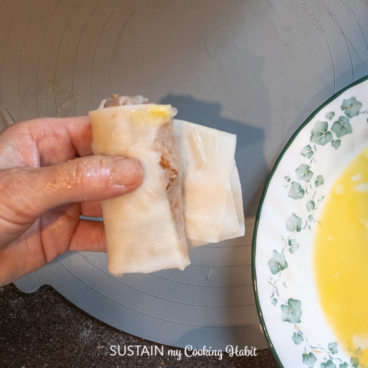 Dipping the end of the pork spring roll into a beaten egg.