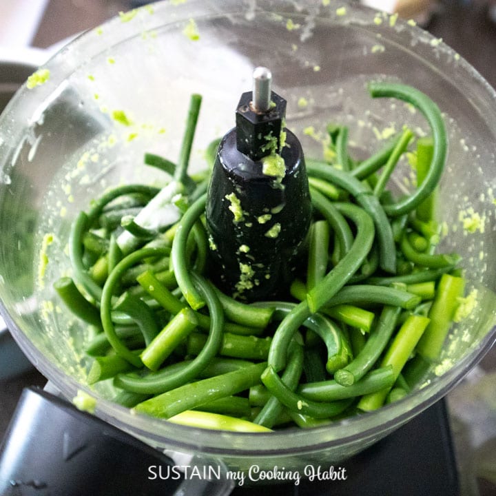 Putting garlic scapes into a food processor.