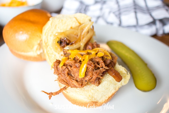 Pulled pork placed on an open bun next to a slice of pickle.