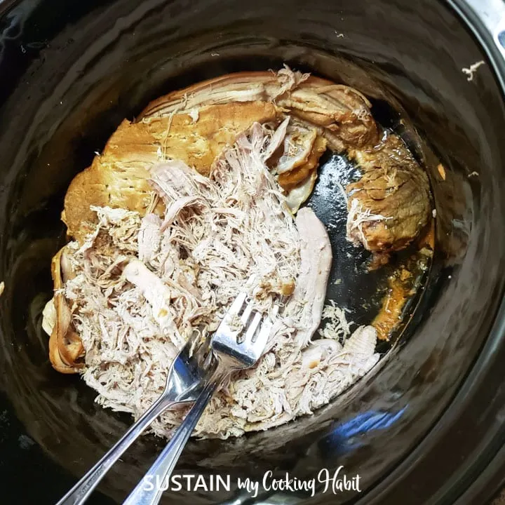 Shredding the pulled pork with forks in the slow cooker.