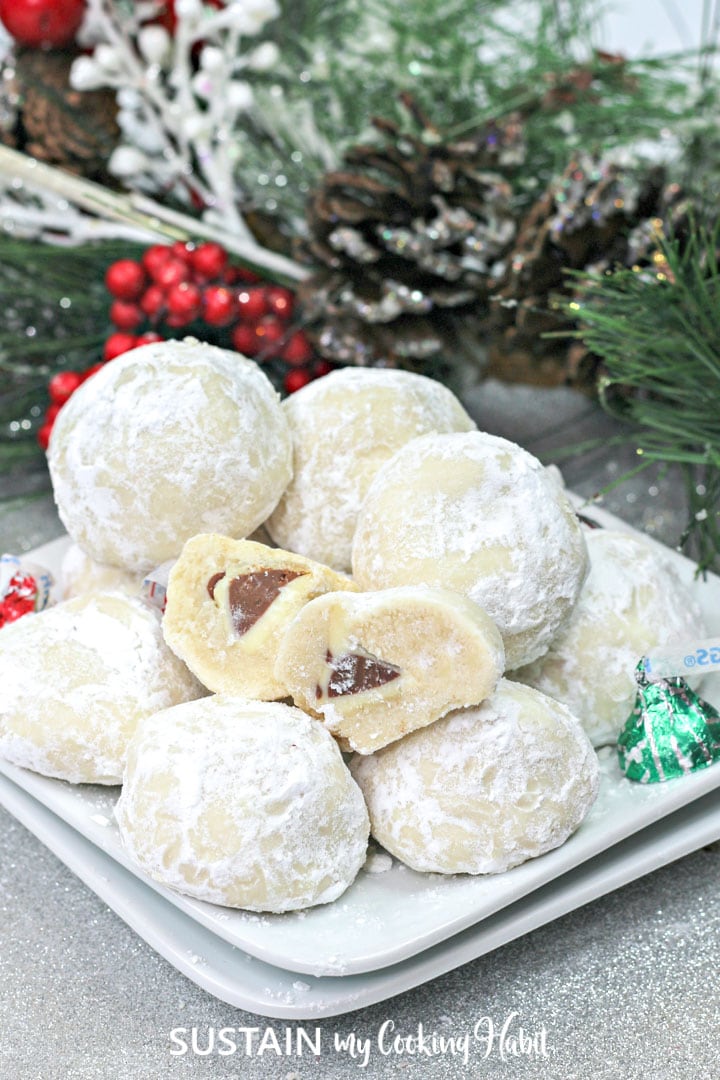 Hershey kiss cookies with a cut open cookie sitting on a white plate next to Hershey kisses.