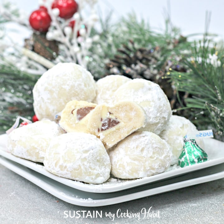 Pile of powdered sugar coated Hershey Kiss cookies on a platter and cut to show chocolate center.