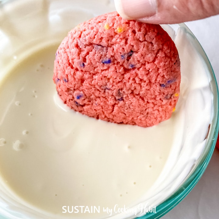 Dipping a strawberry cake mix cookie into the melted chocolate.