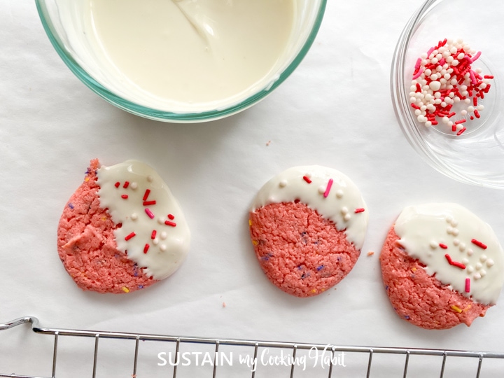 Adding sprinkles to the dipped strawberry cookies.