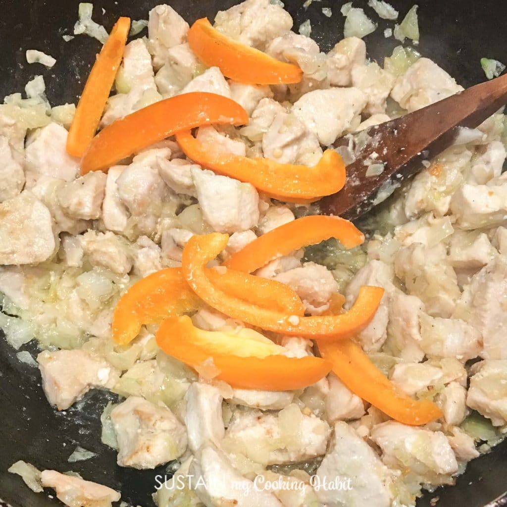 Adding orange peppers to the sauce pan filled with chicken. 