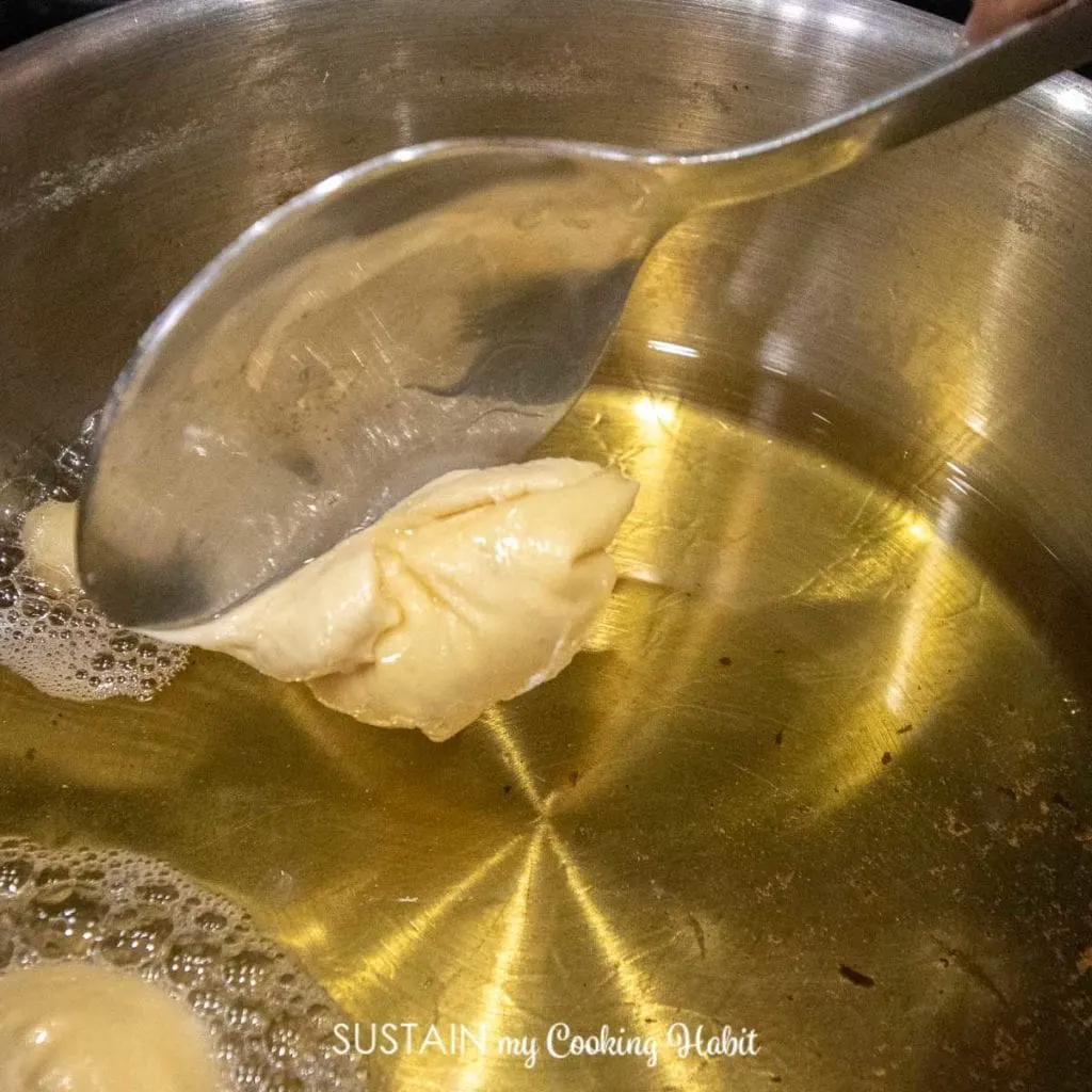 Using a spoon to put dough into a pot of oil.
