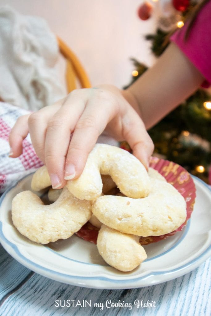 child grabbing one coconut crescent cookie from a plate