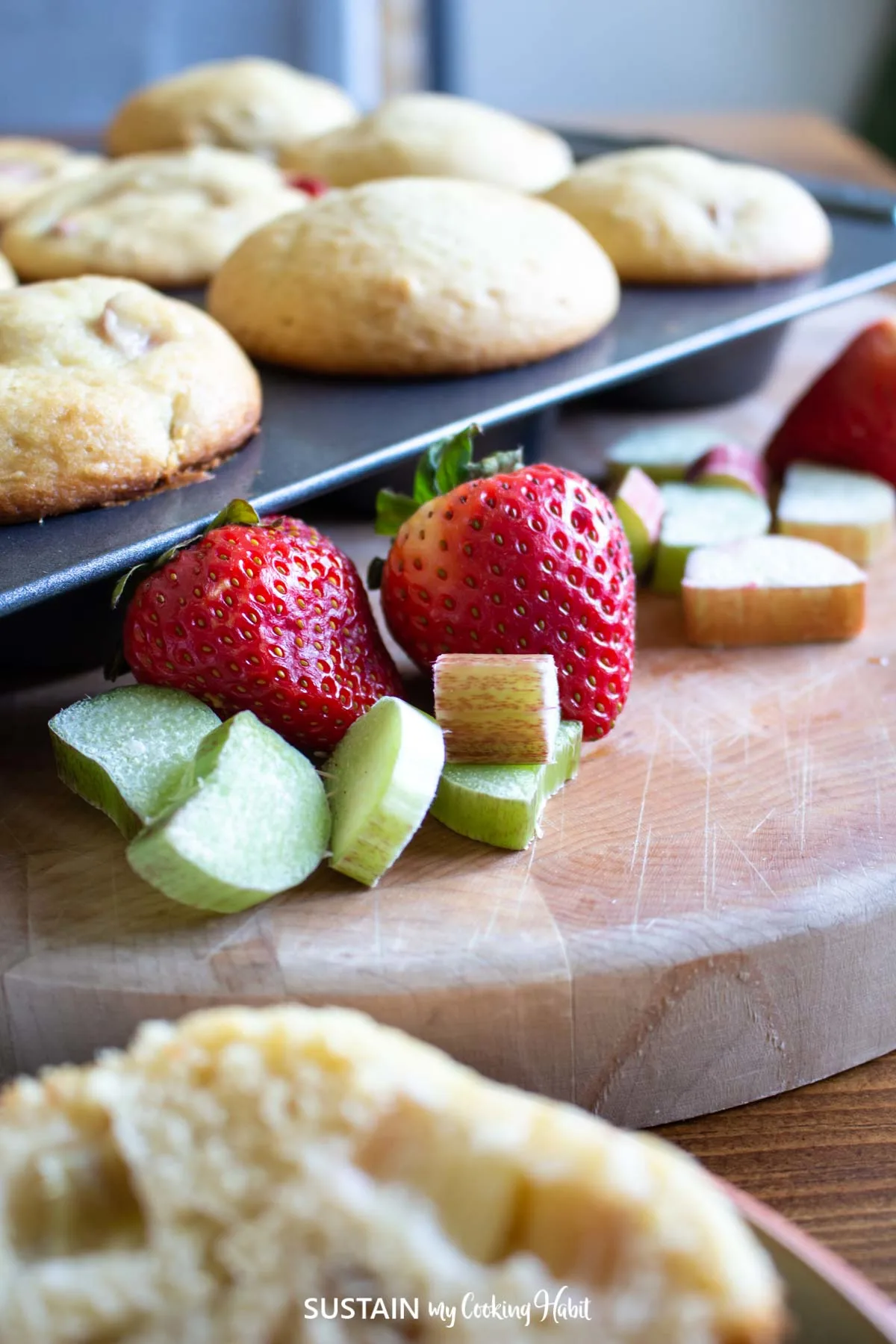 close up image of strawberries and cut rhubarb in front of freshly baked muffins