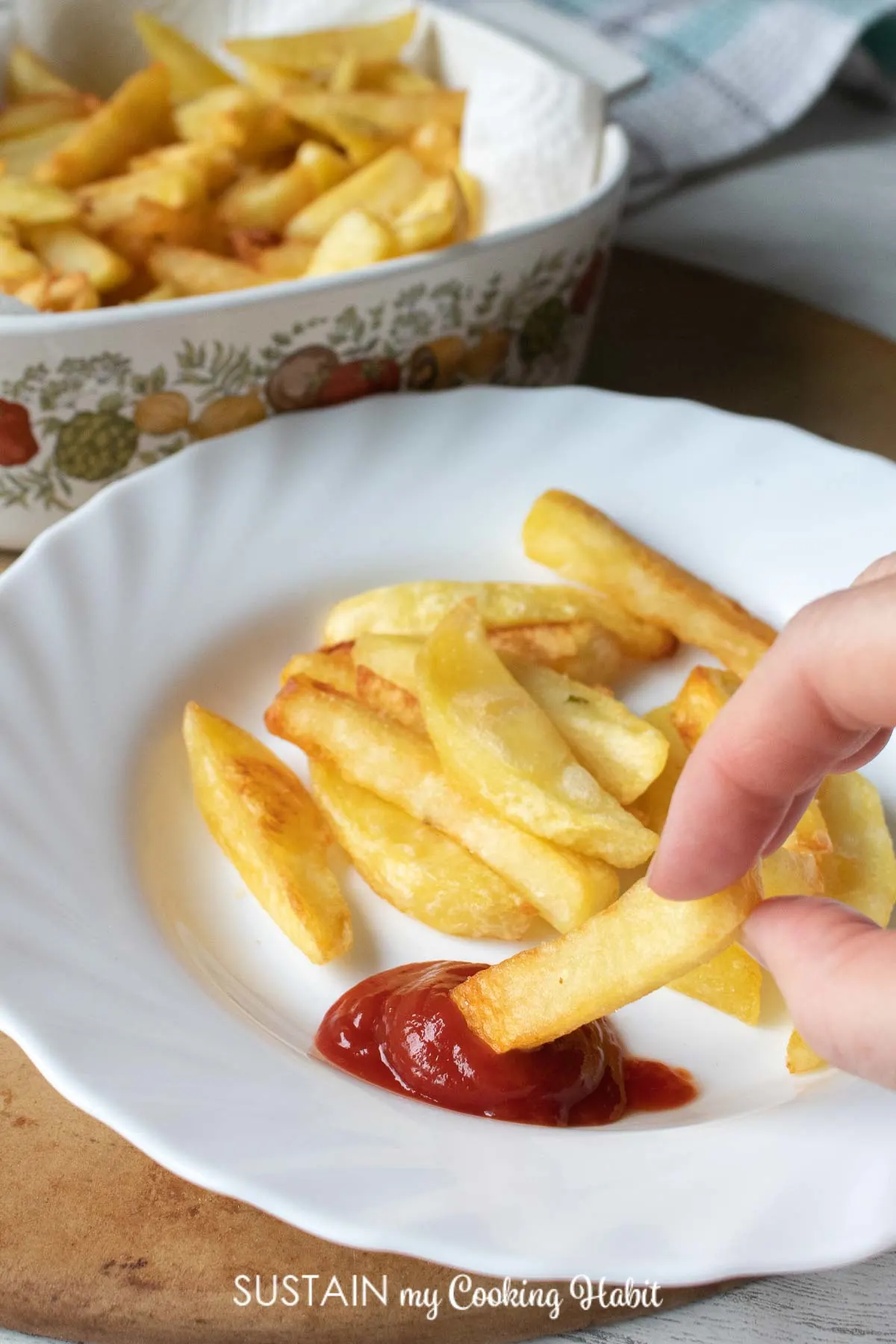 Hand dipping one french fry into ketchup.