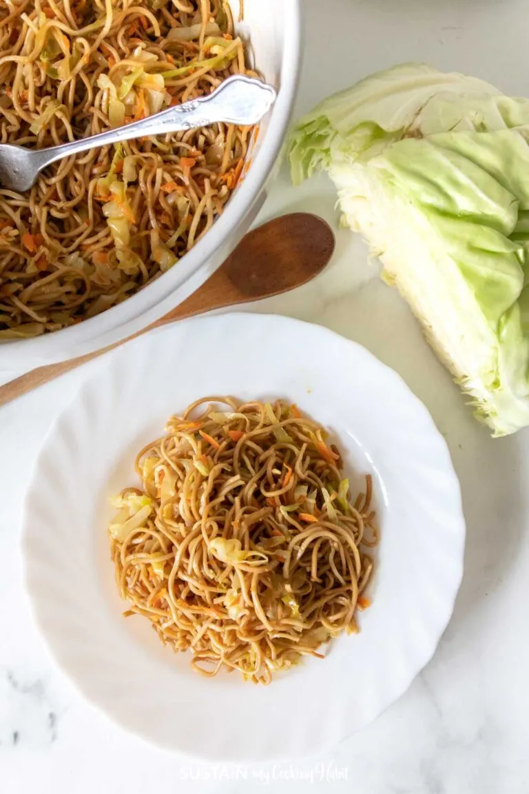 Crispy lo mein noodles plated on white dish with fresh cabbage and wooden spoon nearby.
