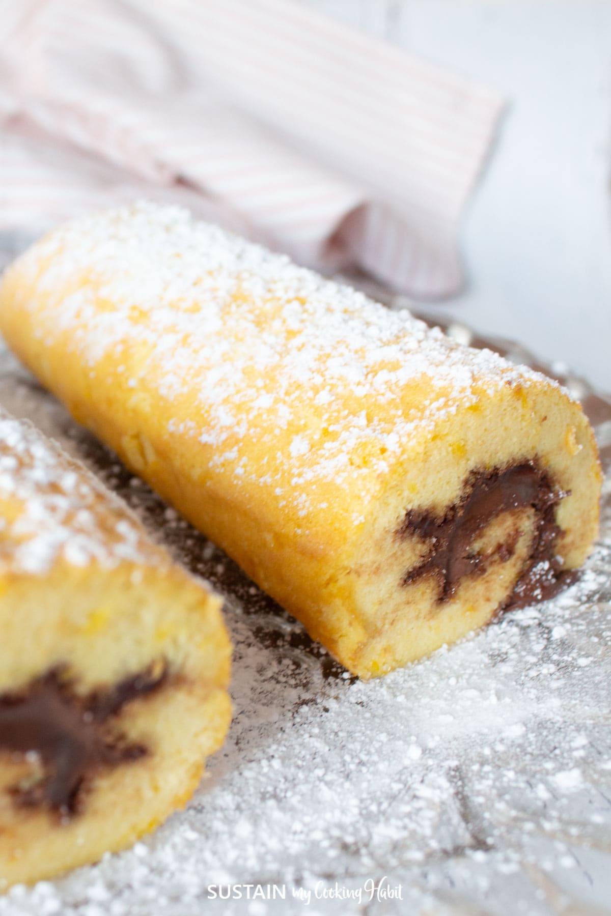 Nutella swiss roll dusted with powder sugar on a plate.