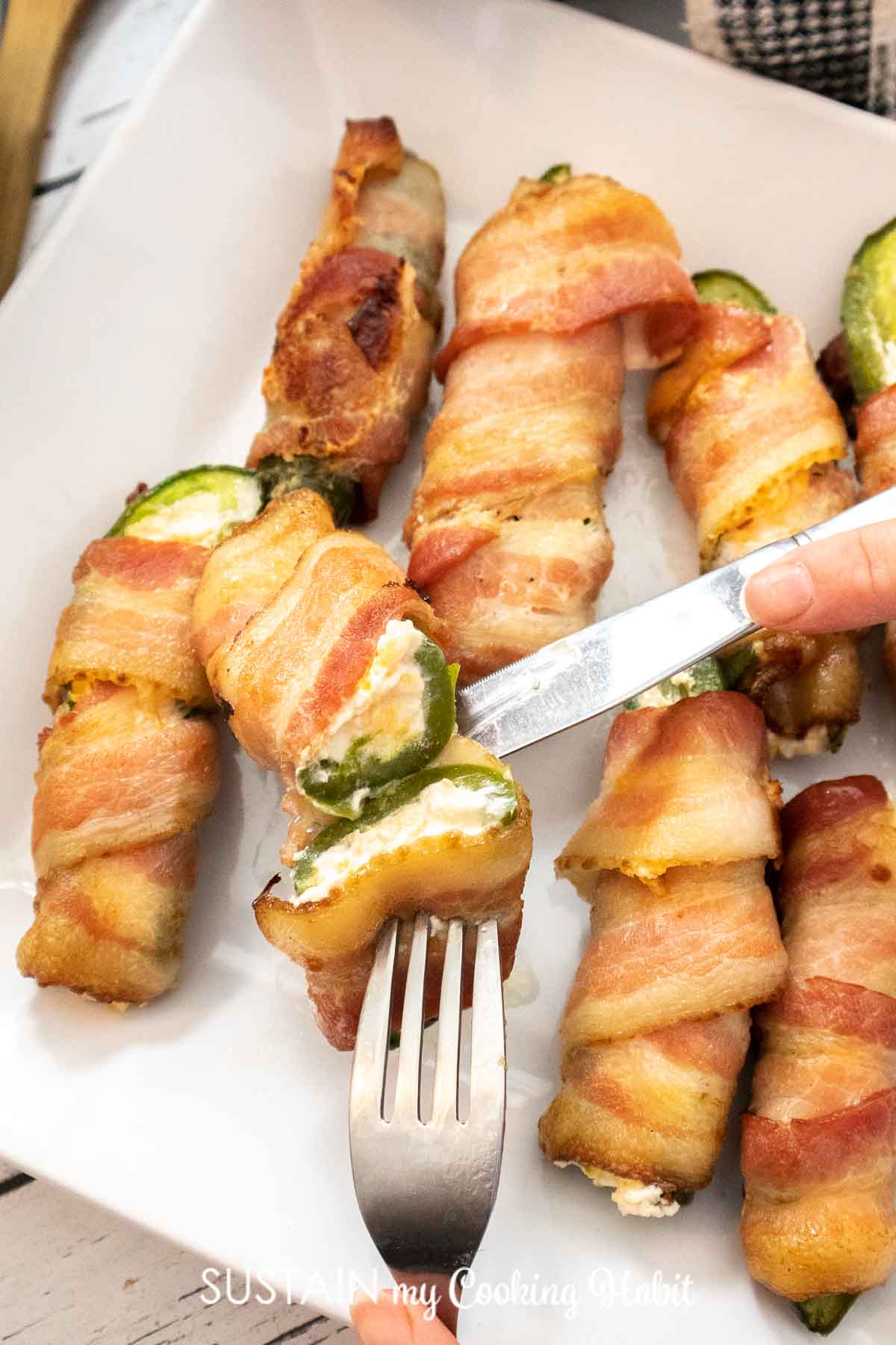 Bacon wrapped jalapeno popper cut open with a fork and knife.