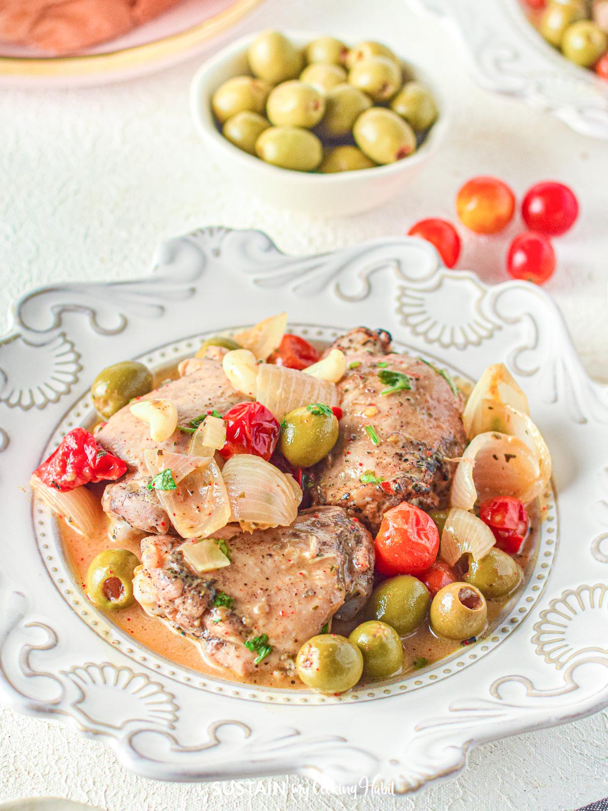 Chicken Provencal in a serving dish next to olives and grape tomatoes.
