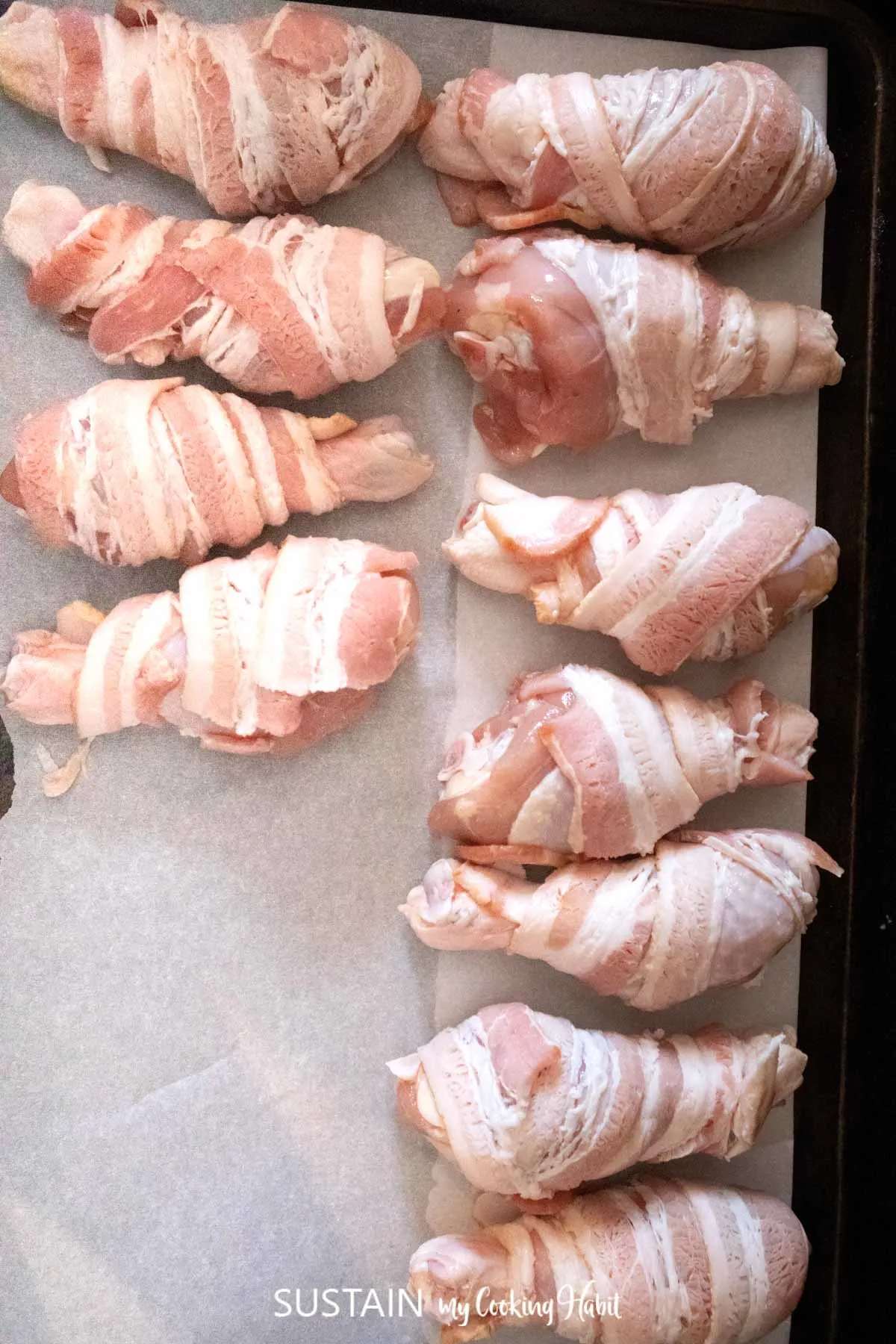 Uncooked bacon wrapped around chicken drumsticks.