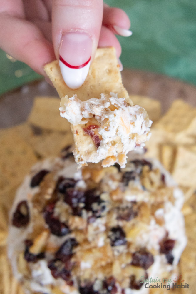 Hand dipping a cracker into the cheese ball.