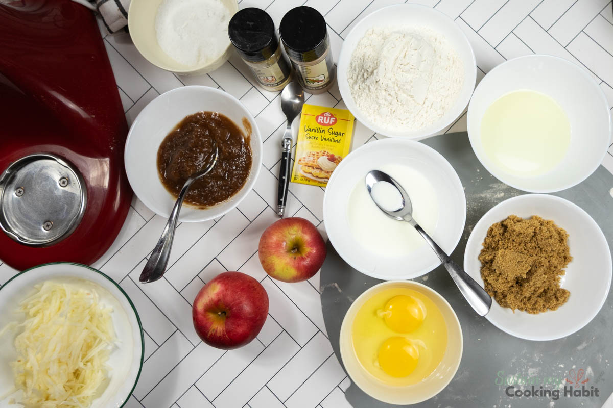 Ingredients needed to make a moist apple cake including apples, flour, sugar, eggs, butter and spices. 
