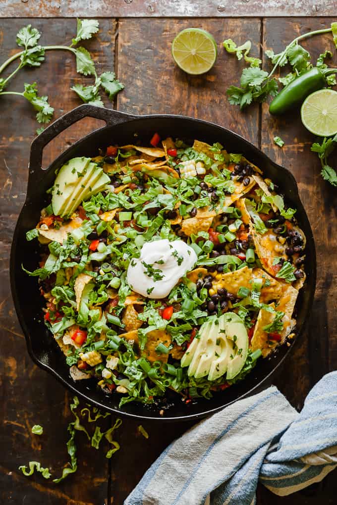 skillet filled with loaded nachos topped with green onions, cheese and sour cream in the center.