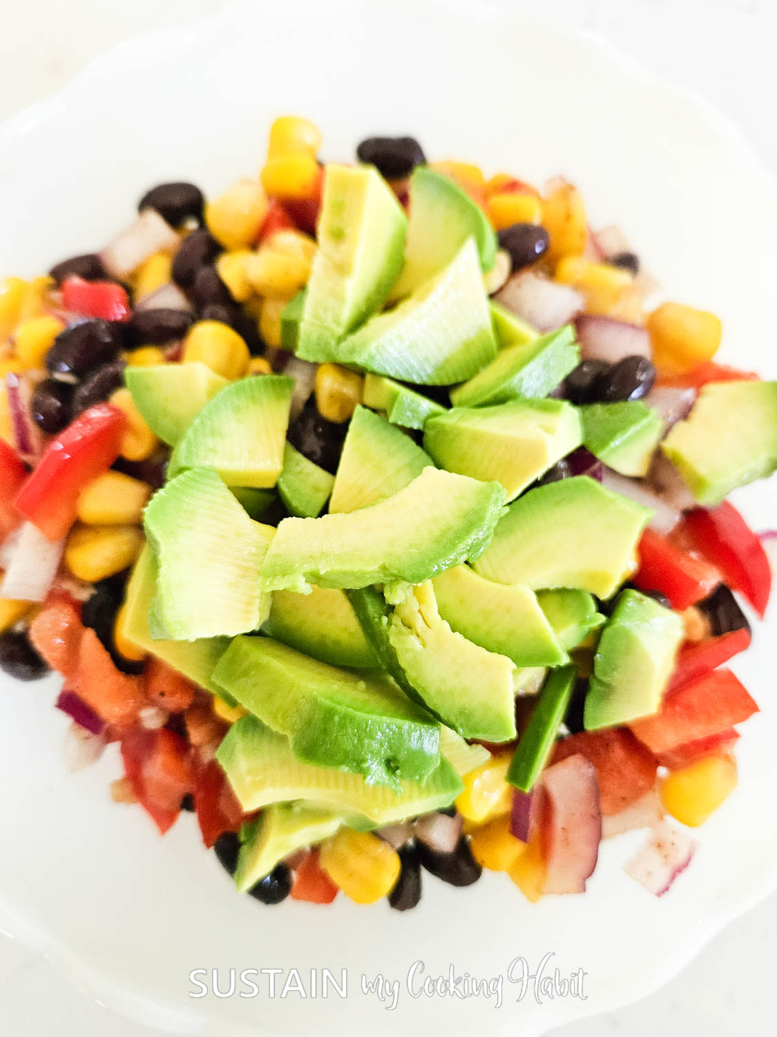 Adding chopped avocados to mixed vegetables. 