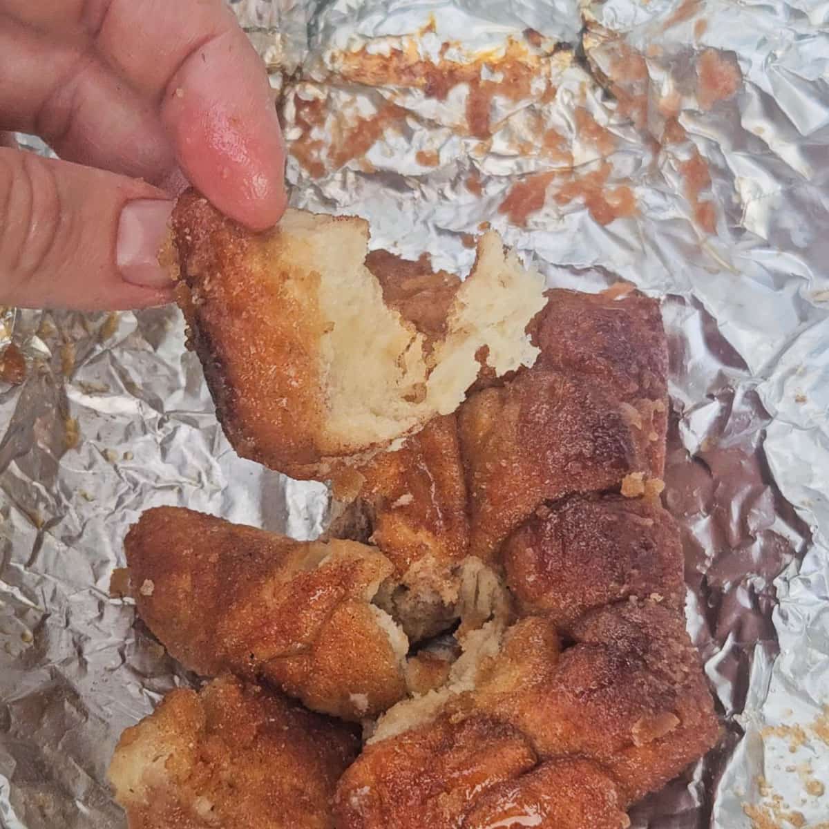 hand pulling apart a loaf of monkey bread wrapped in aluminum foil